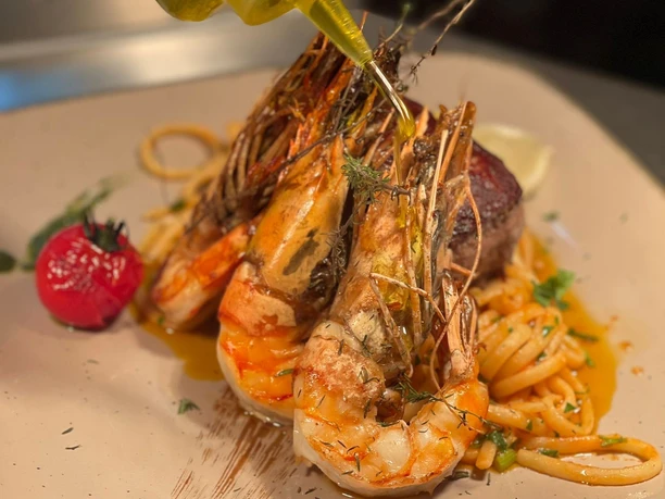 Garnelen mit Kräutern auf Linguine, angerichtet mit gegrillter Tomate, werden mit Olivenöl verfeinert.