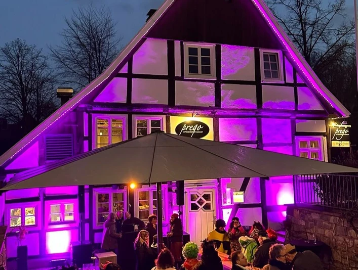 Fachwerkhaus bei Nacht, in lebendigem Lila angestrahlt, mit Besuchern unter einem großen Schirm.