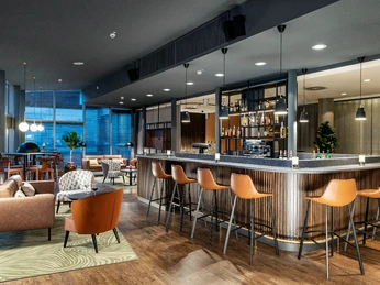 NH_köln-altstadt Moderne Hotelbar mit stilvollen Sitzgelegenheiten, großen Fenstern und elegant beleuchteter Theke.</p>Modern hotel bar with stylish seating, large windows and elegantly lit bar.</p> <p