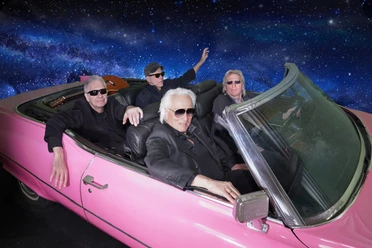 Hannes Schöner Band Vier ältere Männer in Sonnenbrillen fahren in einem pinken Cabrio durch eine Galaxie-Kulisse.