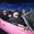 Hannes Schöner Band Vier ältere Männer in Sonnenbrillen fahren in einem pinken Cabrio durch eine Galaxie-Kulisse.Four older men in sunglasses drive through a galaxy backdrop in a pink convertible.