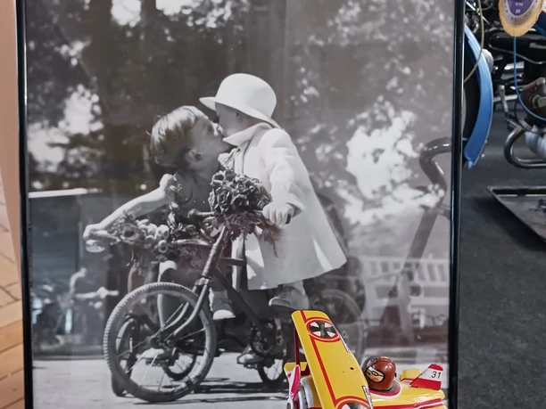Sonderausstellung Schwarzweißfoto von zwei Kindern auf Fahrrädern, die sich in einem Garten küssen.