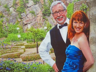 Two people, smiling, pose in front of a lushly planted, terraced rock garden.