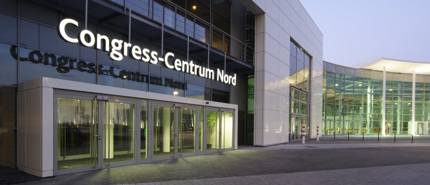Congress-Centrum Nord Koelnmesse, Eingang Congress-Centrum Nord in Köln, modernes Gebäude bei Dämmerung, mit großen Glasfenstern und hellem Eingang.