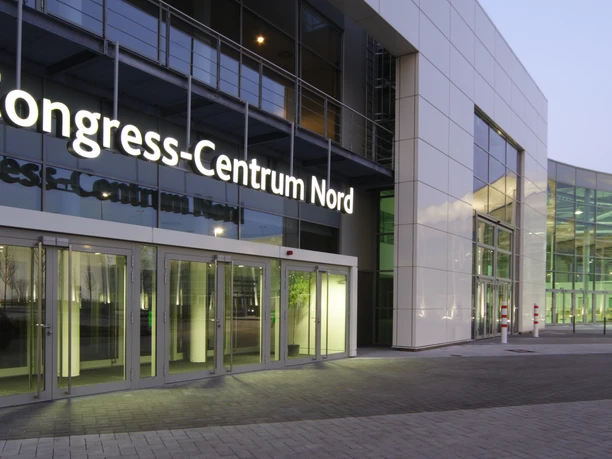 Congress-Centrum Nord Koelnmesse, Entrance Congress-Centrum Nord in Cologne, modern building at dusk, with large glass windows and bright entrance.
