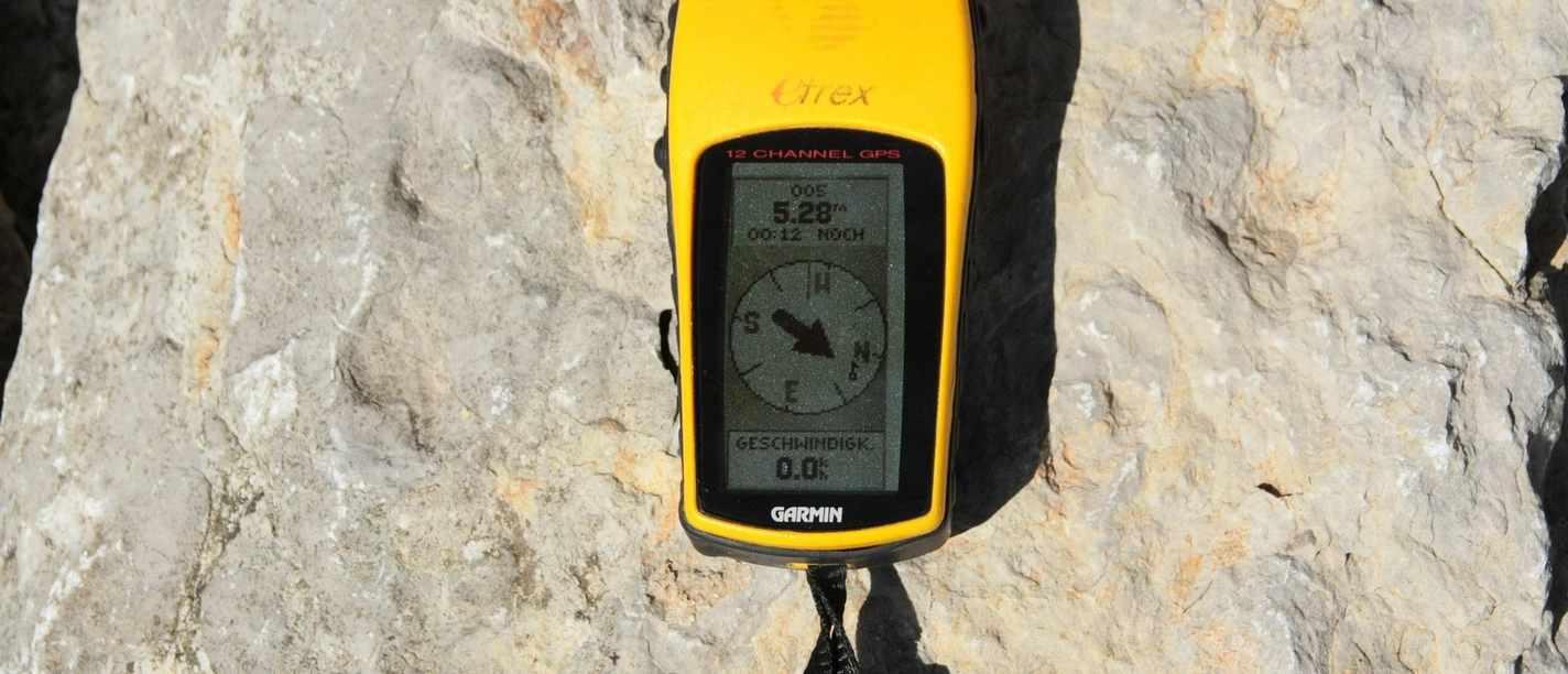 GPS.jpg Leuchtend gelbes, tragbares GPS-Gerät liegt auf einem Felsen in der Sonne. Bildschirm zeigt Kompass.</p>