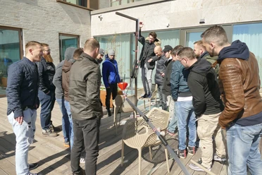 Kugelbahn_Hauptmotiv.jpg Eine Gruppe von Männern baut gemeinsam eine kreative Konstruktion auf einer Holzterrasse.