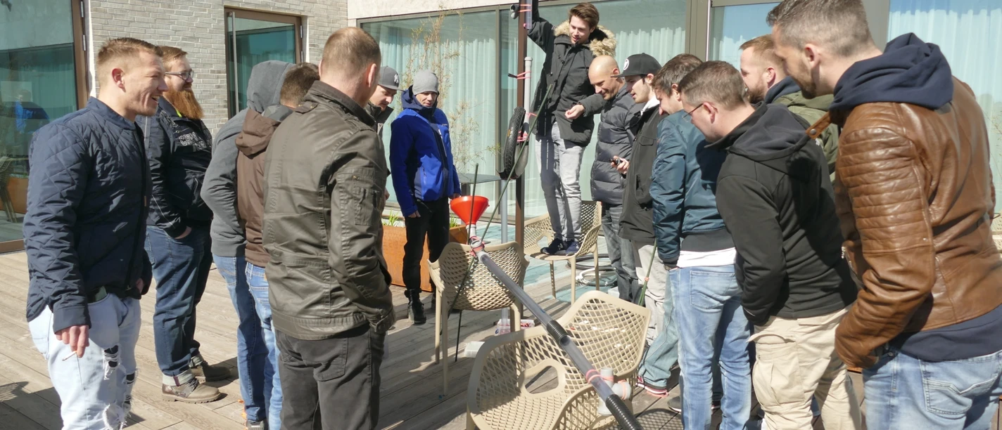 Kugelbahn_Hauptmotiv.jpg Eine Gruppe von Männern baut gemeinsam eine kreative Konstruktion auf einer Holzterrasse.