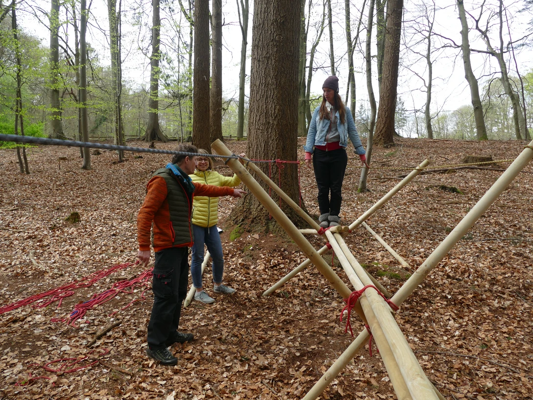 Brückenbau_kreativ.JPG Menschen balancieren auf einem Holzparcours im Wald unter Anleitung, umgeben von Laub auf dem Boden.</p>People balance on a wooden course in the forest under supervision, surrounded by foliage on the ground.</p> <p