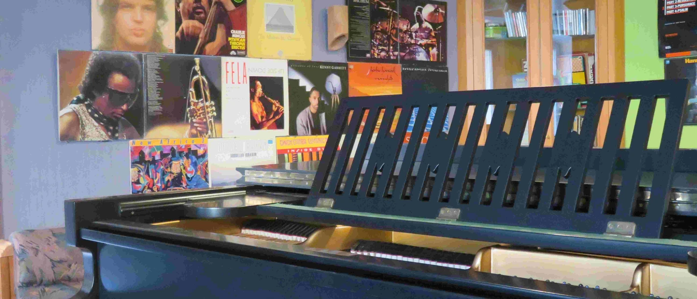 Een vleugel staat voor een muur versierd met platen van beroemde jazzmuzikanten.