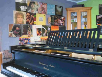 Veranstaltung im "Schuberts" Ein Flügel steht vor einer mit Schallplatten dekorierten Wand, die berühmte Jazzmusiker zeigt.