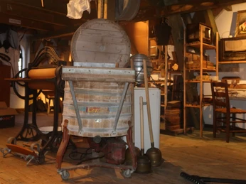 Alte Wäscherei-Maschinen in einem historischen Raum mit Holzboden und diversen Utensilien ausgestellt.