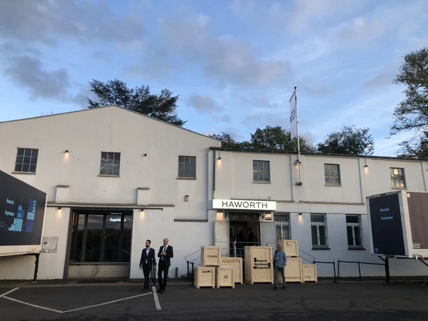 Hafen 12 Graues Gebäude bei Abenddämmerung, Menschen davor, blauer Himmel mit Wolken.</p>