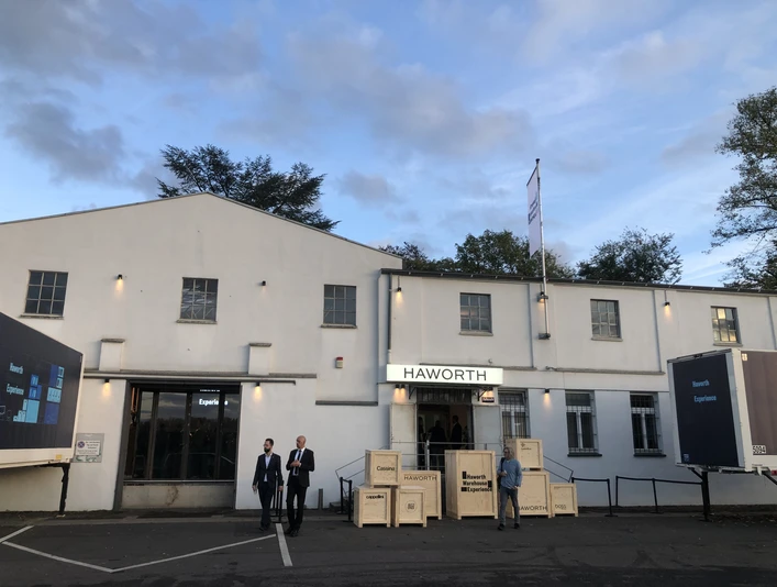 Hafen 12 Graues Gebäude bei Abenddämmerung, Menschen davor, blauer Himmel mit Wolken.</p>Gray building at dusk, people in front of it, blue sky with clouds.</p> <p