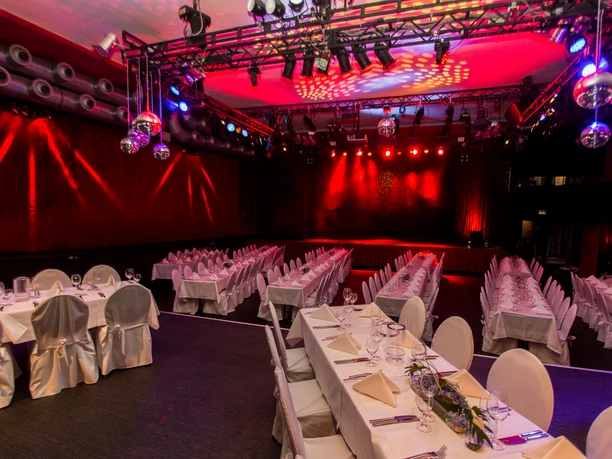 Banquet event with festively decorated tables, red stage lighting and shiny mirror balls.