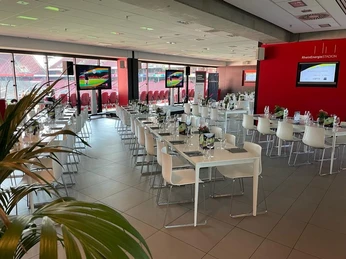 Business-Veranstaltung Elegante Veranstaltungslocation mit gedeckten Tischen, Monitoren und Panoramablick auf ein Stadion.</p>Elegant event location with set tables, monitors and a panoramic view of a stadium.