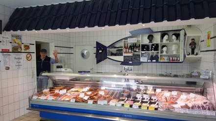 Allräucherei Prahm-Theke-Apen.jpg Ein Verkäufer in weißem Kittel grüßt freundlich hinter einer gut bestückten Fischtheke.