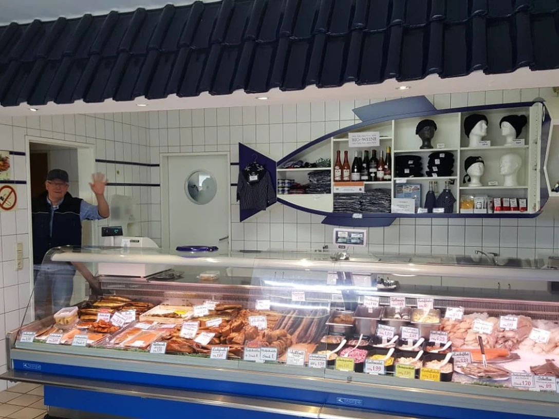 Allräucherei Prahm-Theke-Apen.jpg Ein Verkäufer in weißem Kittel grüßt freundlich hinter einer gut bestückten Fischtheke.