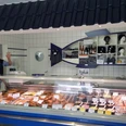 Allräucherei Prahm-Theke-Apen.jpg Ein Verkäufer in weißem Kittel grüßt freundlich hinter einer gut bestückten Fischtheke.