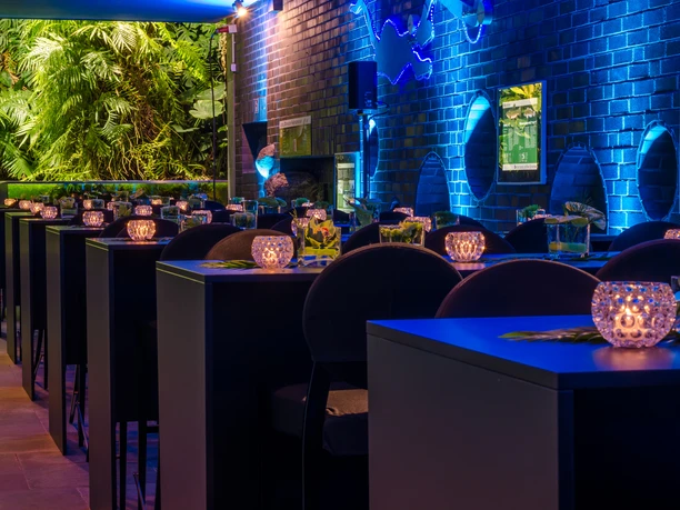 Aquarium Bar im modernen Stil mit stimmungsvoller Beleuchtung und dekorativen Kerzen auf den Tischen.