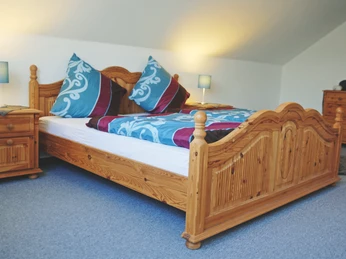 Ein geräumiges Doppelzimmer mit einem holzgeschnitzten Bett, farbiger Bettwäsche und Nachttischen.