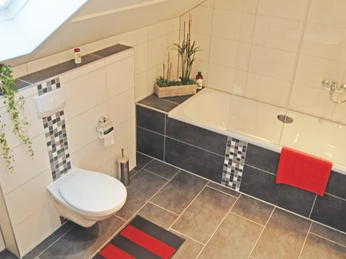 Modernes Badezimmer mit einer Badewanne, weißen Fliesen, grauen Akzenten und dekorativen Pflanzen.