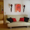 Ferienwohnung Hoppe_SchZi_c_SHS.jpg Ledersofa mit rot-schwarzen Kissen vor weißer Wand, dekoriert mit Rosenbild und zwei Kerzenhaltern.