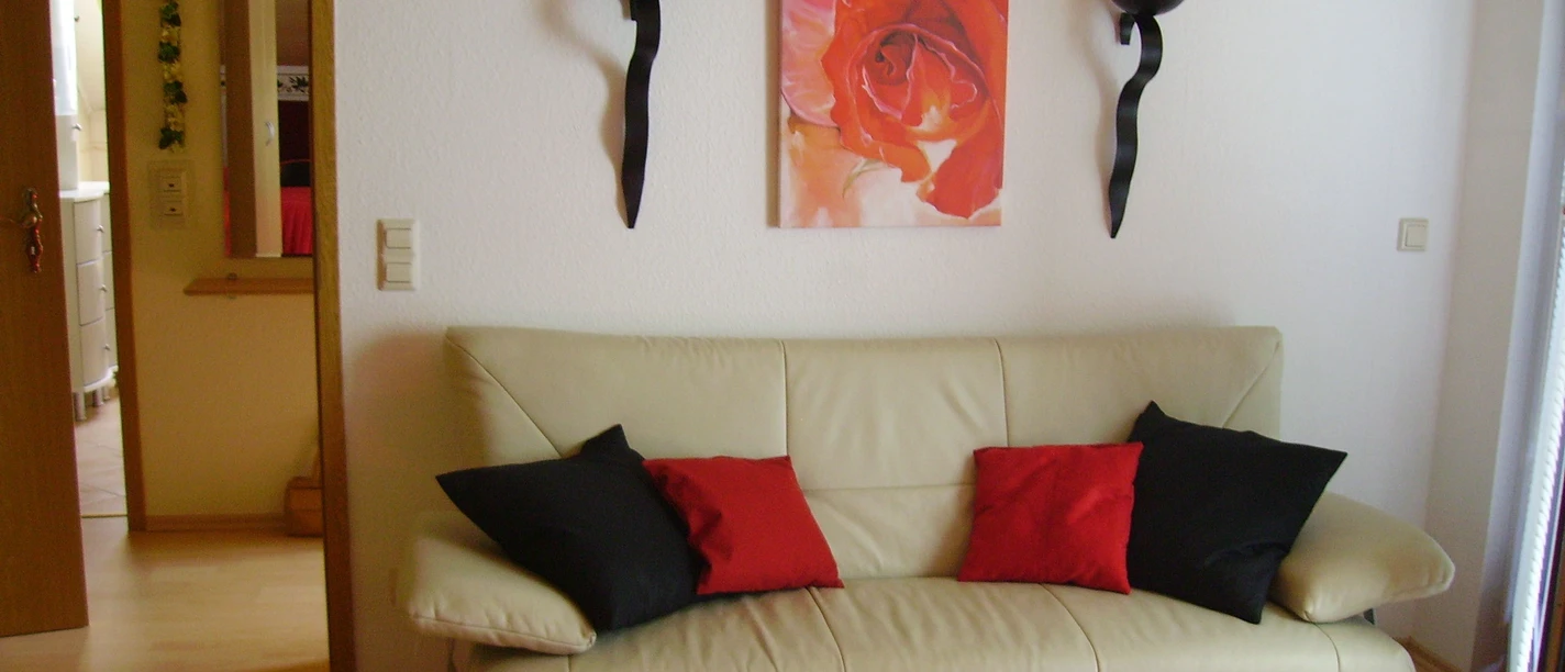 Ferienwohnung Hoppe_SchZi_c_SHS.jpg Ledersofa mit rot-schwarzen Kissen vor weißer Wand, dekoriert mit Rosenbild und zwei Kerzenhaltern.