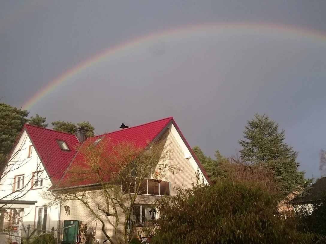 DSC_0232 Herzog.JPG Zweistöckiges Haus mit rotem Dach im Vordergrund, beeindruckender Regenbogen am Himmel darüber.