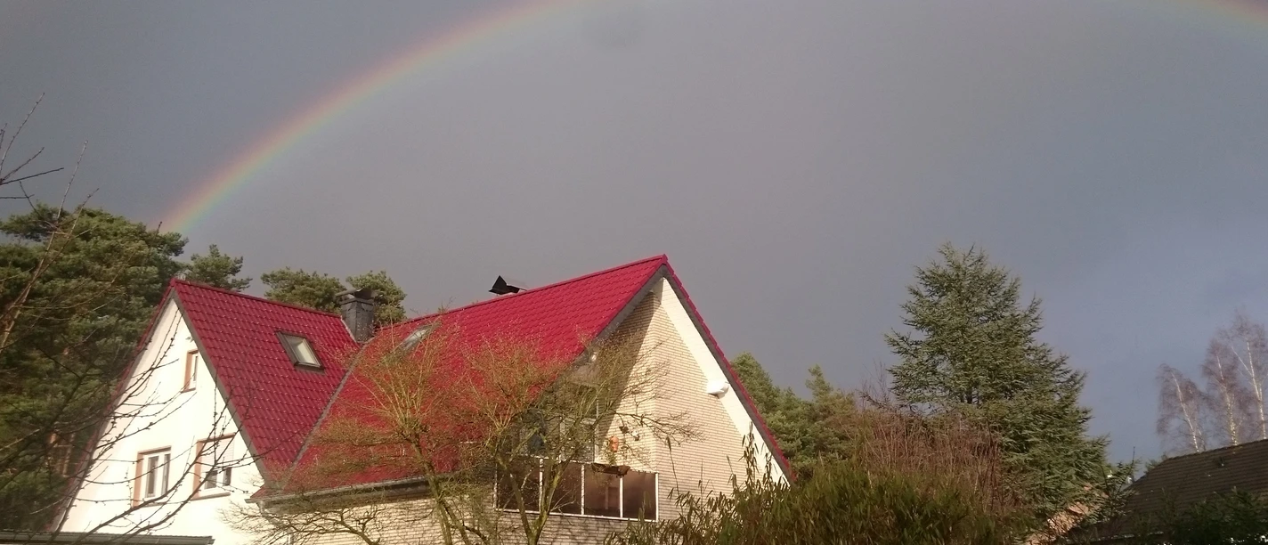 DSC_0232 Herzog.JPG Zweistöckiges Haus mit rotem Dach im Vordergrund, beeindruckender Regenbogen am Himmel darüber.