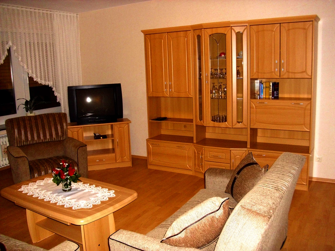 Wernekenschnieder.JPG Eine Wohnzimmer-Einrichtung mit Holzschränken, Sofa, Sessel, Fernseher und Couchtisch in warmen Tönen.