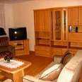 Wernekenschnieder.JPG Eine Wohnzimmer-Einrichtung mit Holzschränken, Sofa, Sessel, Fernseher und Couchtisch in warmen Tönen.