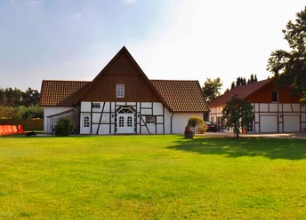Wolfslau.jpg Fachwerkhaus mit Garten und rotem Dach unter klarem Himmel, umgeben von grünem Rasen und Bäumen.