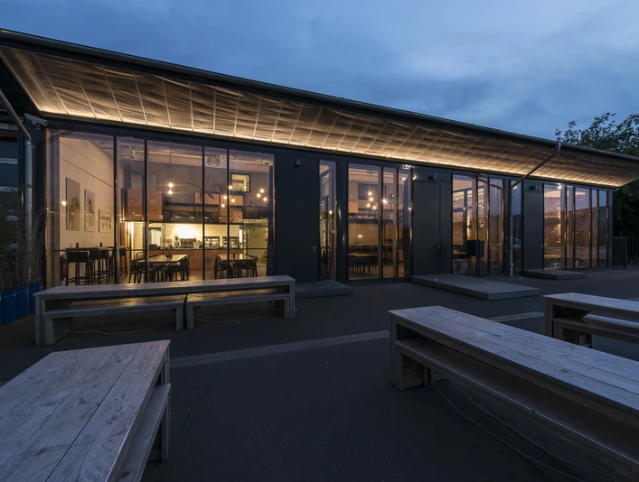 DEINspeisesalon Eventlocation Moderne Glasfassade eines Gebäudes in der Dämmerung, beleuchtet mit warmen Lichtern im Inneren.</p>Modern glass façade of a building at dusk, illuminated with warm lights inside.</p> <p
