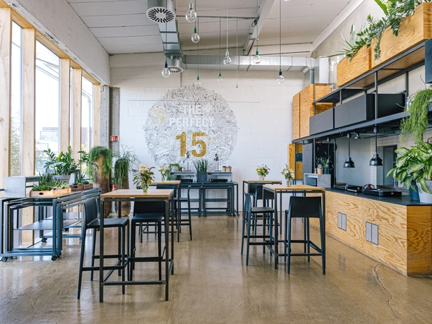 DEINspeisesalon Industrial-chic café with high tables, plants and modern wall decorations in a bright room.