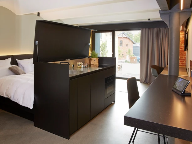 Moderne Studiosuite mit offener Küchenzeile, gemütlichem Doppelbett und Arbeitsplatz mit Blick nach draußen.