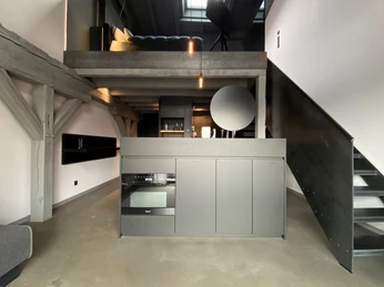 Ueberblick_Loft B+.jpg Moderne, graue Loftwohnung mit offener Küche, sichtbaren Holzbalken und Treppe zur offenen Empore.