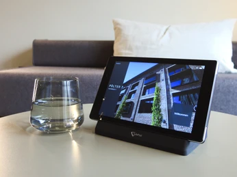 PÖLTER Pad_der digitale Concierge Ein Tablet auf einem Tisch neben einem Glas Wasser zeigt eine moderne Gebäudefassade.