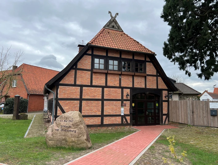 Fachwerkgebäude in Drakenburg mit rotem Ziegeldach, umgeben von Bäumen und Wiesen, historisches Flair.