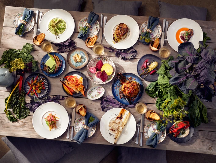 CATERING NEU DENKEN Farbenfrohe, abwechslungsreich angerichtete Speisen auf einem hölzernen Tisch, dekoriert mit Pflanzen.</p>Colorful, varied dishes served on a wooden table, decorated with plants.</p> <p