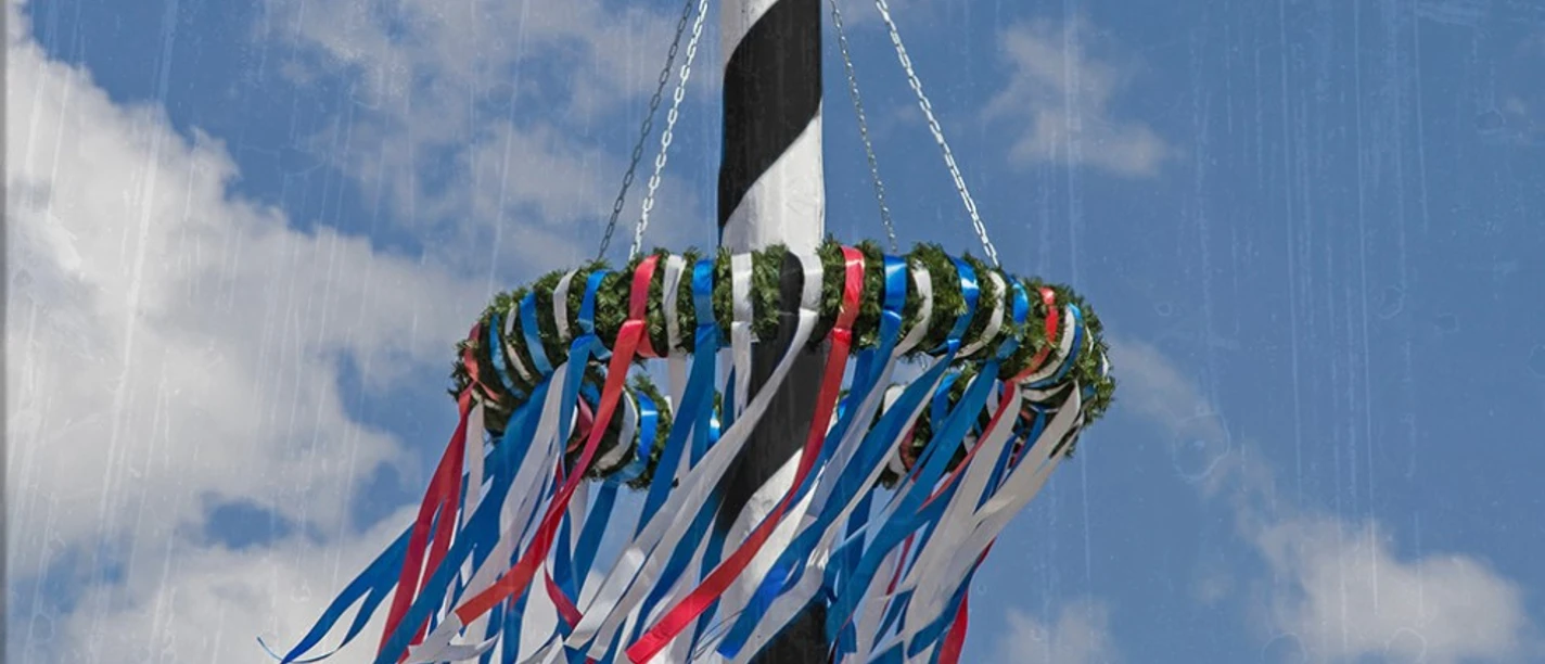 Ein festlich geschmückter Maibaum mit bunten Bändern vor einem strahlend blauen Himmel.