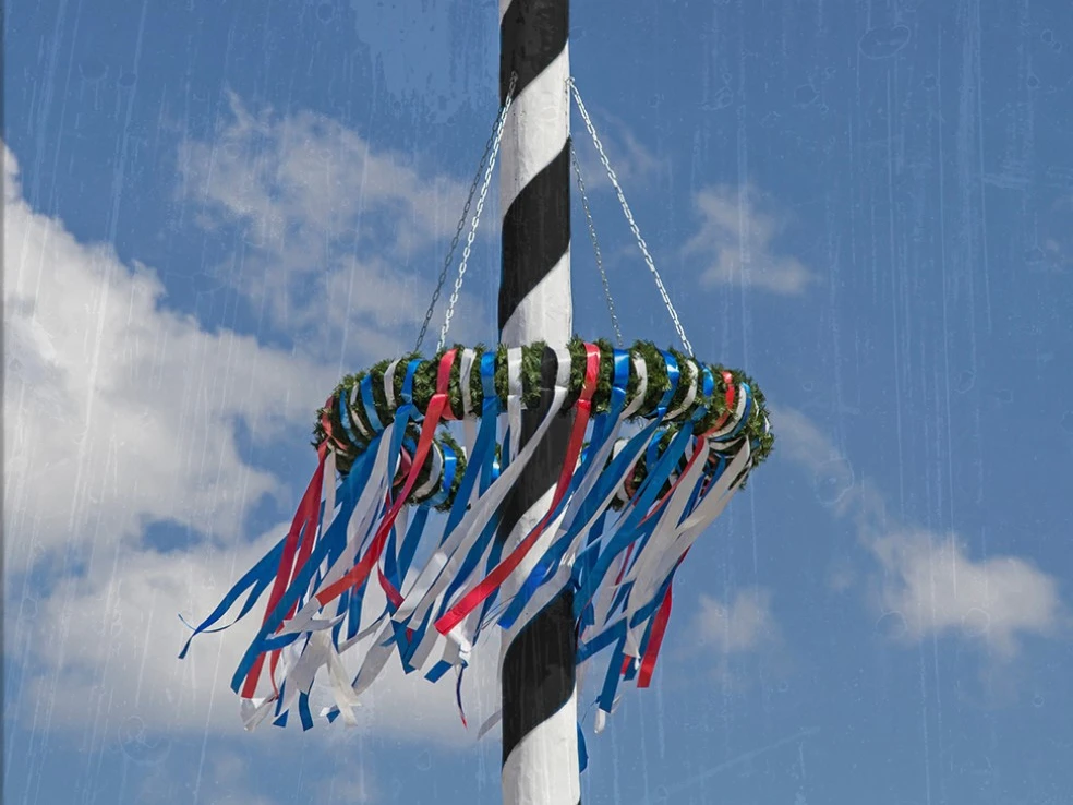 Ein festlich geschmückter Maibaum mit bunten Bändern vor einem strahlend blauen Himmel.
