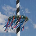 Maibaum.jpg Ein festlich geschmückter Maibaum mit bunten Bändern vor einem strahlend blauen Himmel.