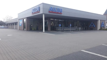 2023-03-19.jpg Das Bild zeigt eine ALDI-Filiale mit weitläufigem Parkplatz, Einkaufswagenbereich und moderner Fassade.