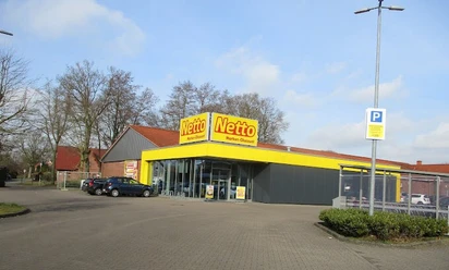 Netto_Apen_2023.jpg Außenansicht eines Netto-Markts in Apen, Parkplatz und Einkaufswagenbereich.