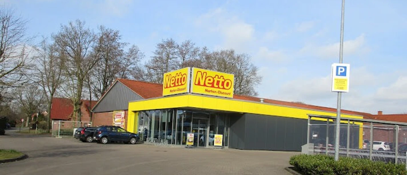 Netto_Apen_2023.jpg Außenansicht eines Netto-Markts in Apen, Parkplatz und Einkaufswagenbereich.