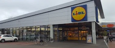 Lidl_Augustfehn_2023.jpg Ein moderner Lidl-Supermarkt mit großem Parkplatz, Fahrradständern, klarer Architektur und dem markanten, blau-gelben Logo.