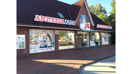 Apotheke-Apen_2023.jpg Das Bild zeigt die Frontansicht der Apotheke Apen mit einem markanten roten Schriftzug auf dem Dach. Die Fassade ist aus roten Backsteinen und verfügt über große Fenster, die Einblicke ins Innere gewähren. Vor der Apotheke befindet sich ein breiter Gehweg mit Pflastersteinen, begleitet von grünen Pflanzen in Töpfen. Die Apotheke strahlt eine einladende Atmosphäre aus.