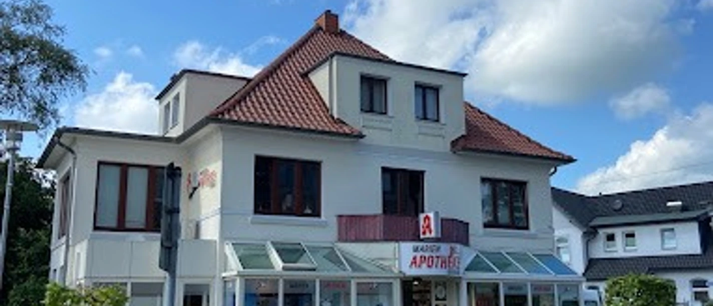 Marien-Apotheke_Augustfehn_2023.jpg Ansicht der Marien-Apotheke Augustfehn, ein zweistöckiges, weißes Gebäude mit roten Dachziegeln.