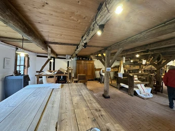 Innenansicht einer historischen Holzmühle mit Holzbalken, alten Geräten und Arbeitsflächen.